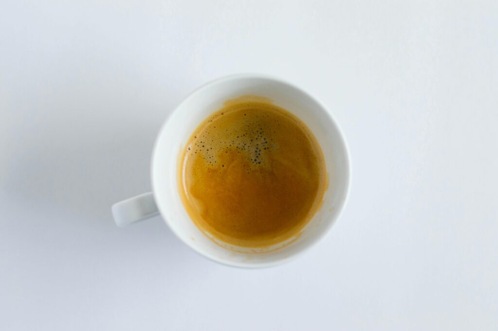 Minimalist top-down photo of a steaming cup of espresso in a white mug against a white background.